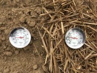 photo of two thermometers, one in bare soil and one in soil with residue cover